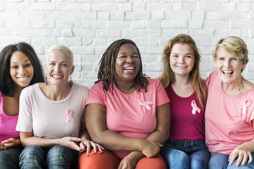 5 women sitting with breast cancer shirts laughing